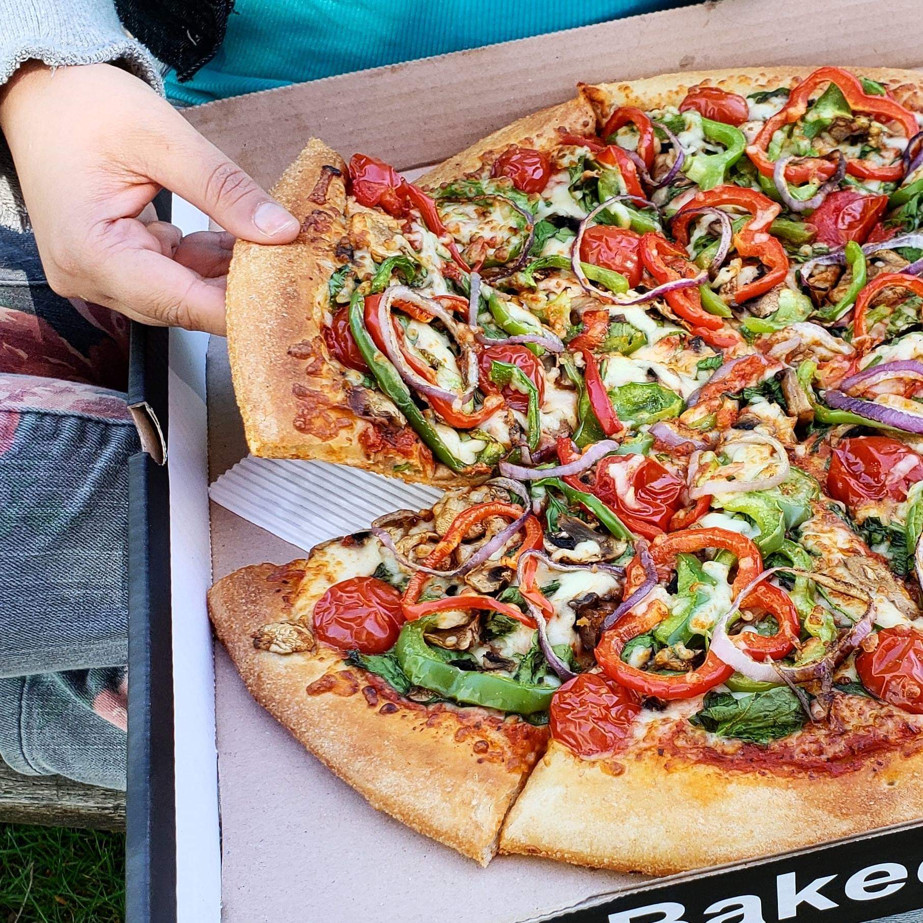 large pizza in box with hand removing a slice