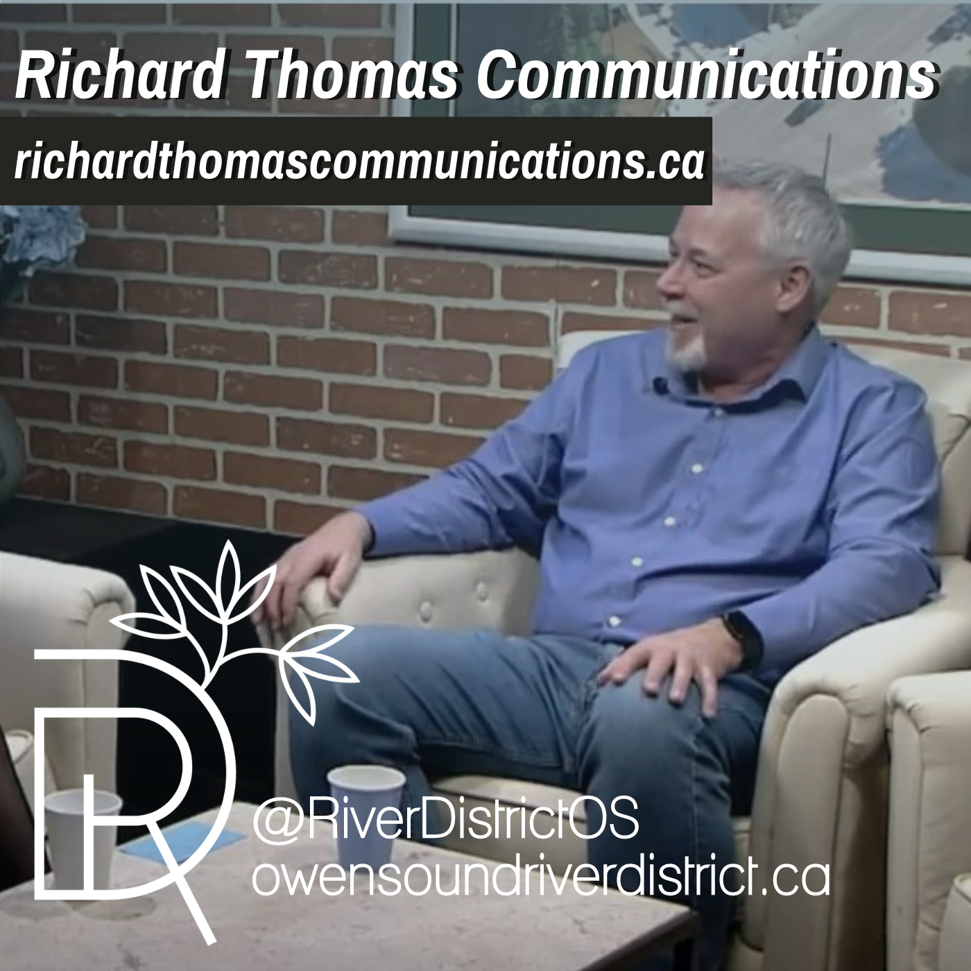 richard thomas in white chair in front of a faux brick wall and large white framed areal image of owen sound