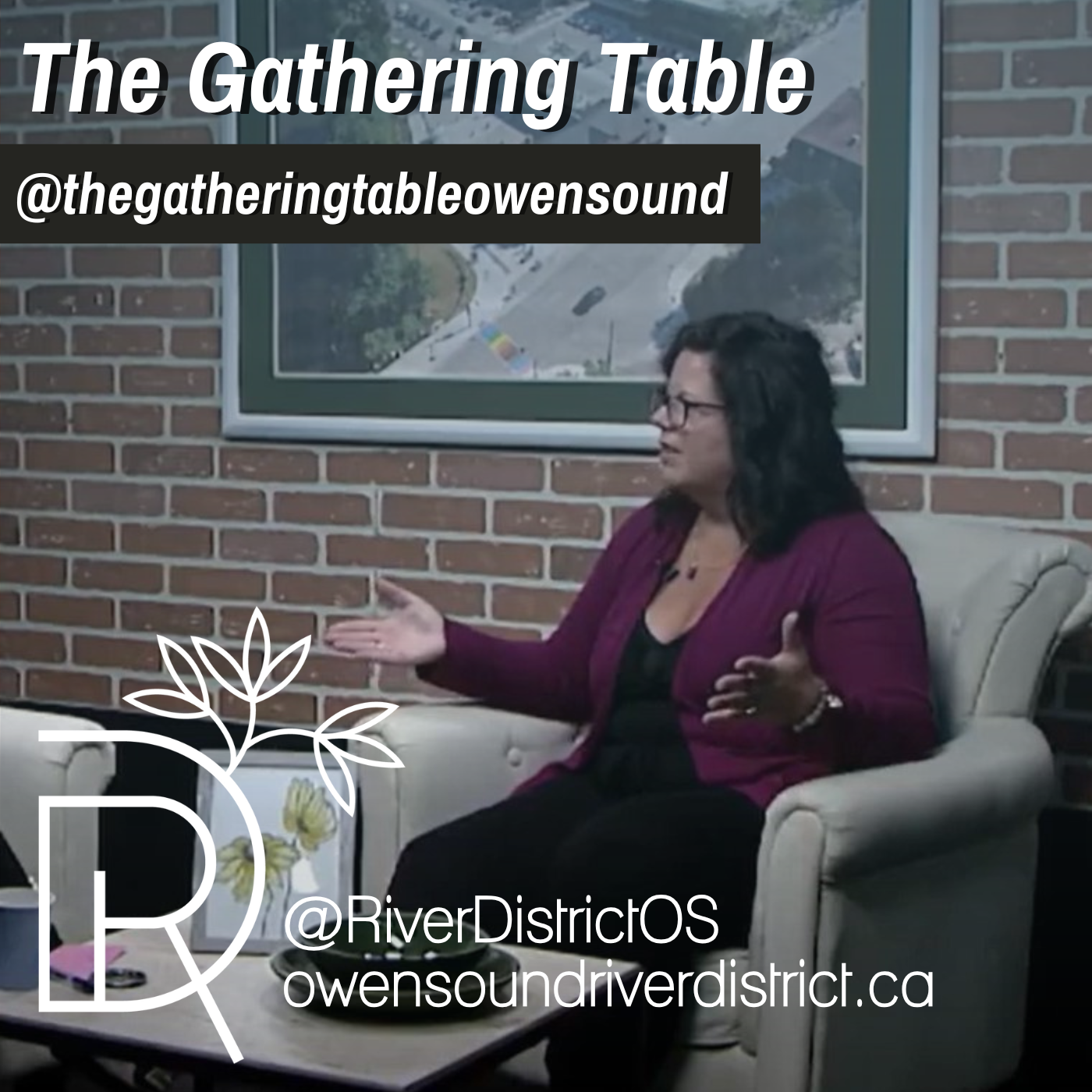 Woman with dark hair and purple sweater sitting in white chair against a faux brick wall and large photo of a city scape